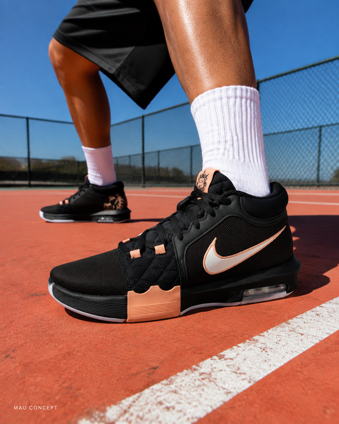 Чёрный кроссовок с белым swoosh и персиковыми деталями крупно у камеры на коралловом покрытии; белый носок и жёсткая тень